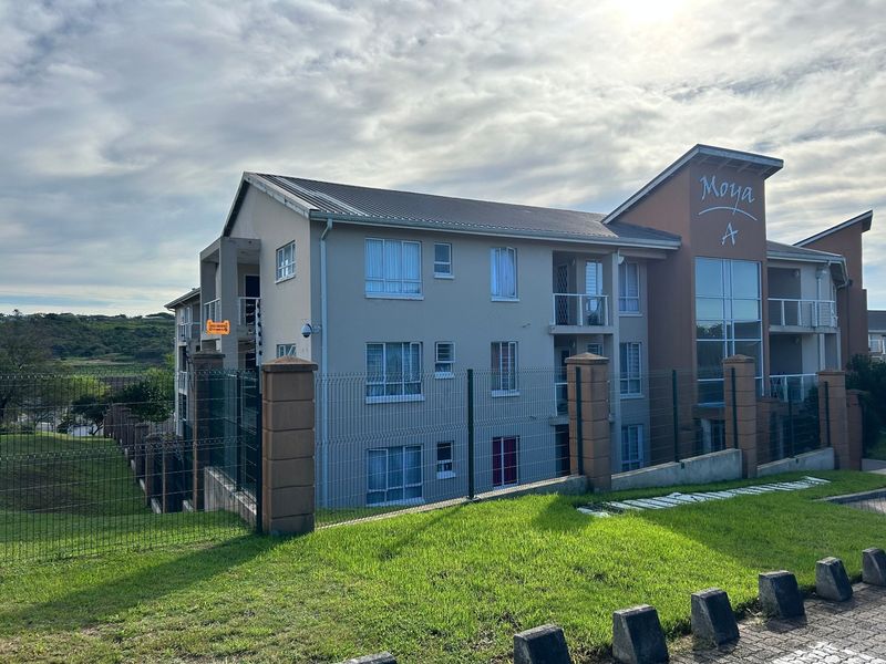 Exterior view of the Moya A apartment complex, featuring a multi-story building with balconies, secure perimeter fencing, and well-maintained grounds.
