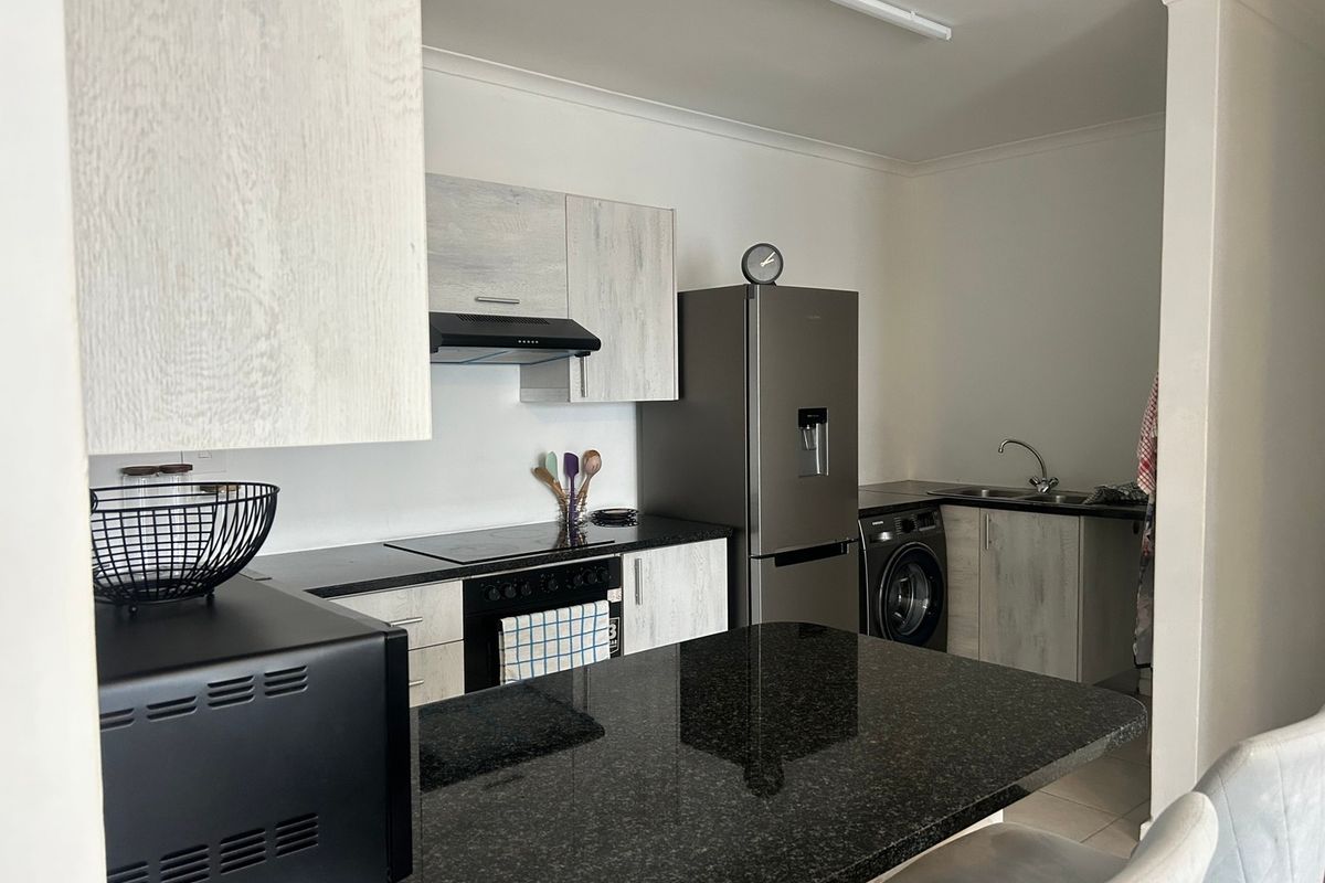 Modern kitchen featuring granite countertops, built-in oven, electric hob, extractor fan, and integrated cabinetry with a functional layout.