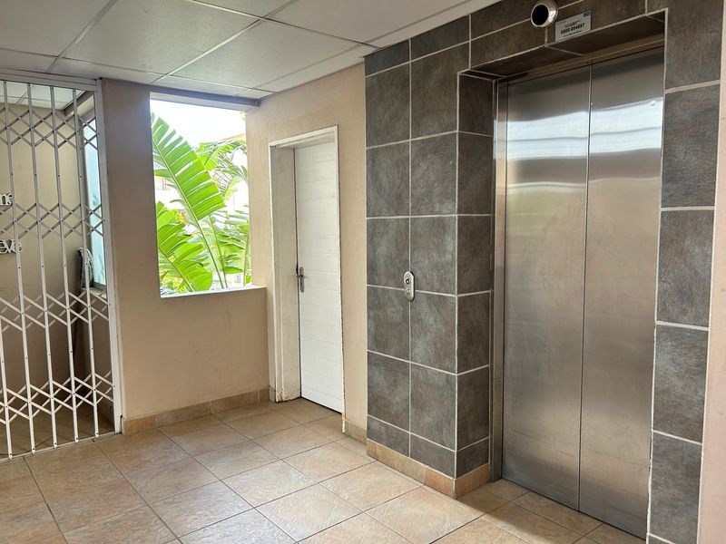 A clean apartment building hallway featuring a stainless steel elevator, tiled flooring, and secure access gate.