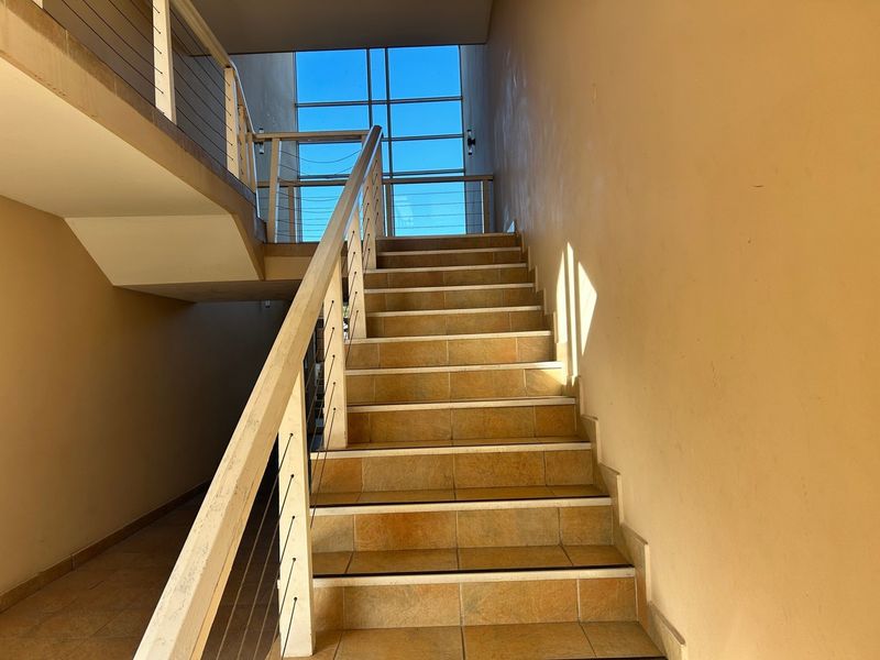 A bright, tiled staircase featuring a metal balustrade and a large window, providing natural light to the apartment building's common hallway area.