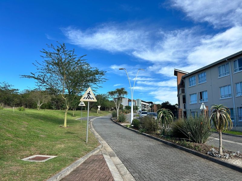 A view of the paved access road and landscaped grounds leading to the apartment complex, featuring street lighting and clear pedestrian signage.