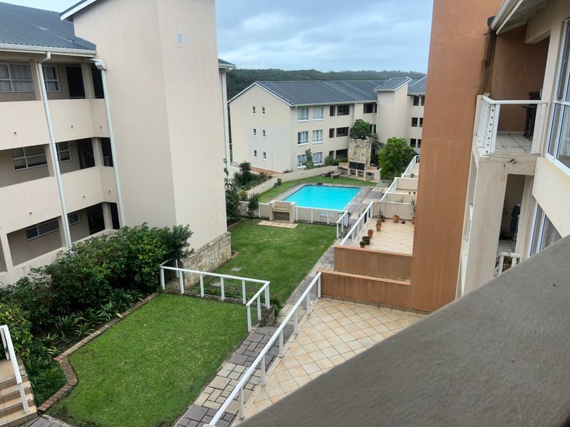 Elevated view of the apartment complex grounds featuring a communal swimming pool, landscaped garden areas, and paved patio spaces.