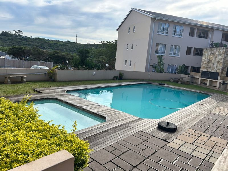 Outdoor pool area featuring a swimming pool, wooden decking, paved patio, and a built-in braai with stone cladding.