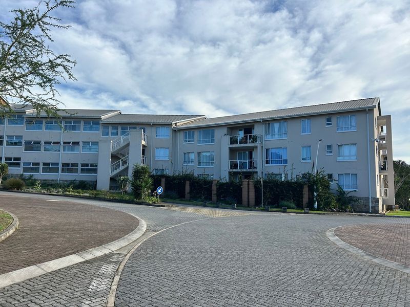 A view of the apartment complex exterior featuring paved driveway access, multi-level balconies, and external staircases under a clear sky.