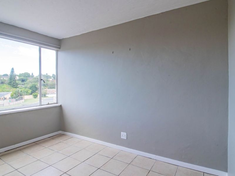 An empty bedroom featuring tiled flooring, a large window with neighborhood views, and neutral wall finishes.
