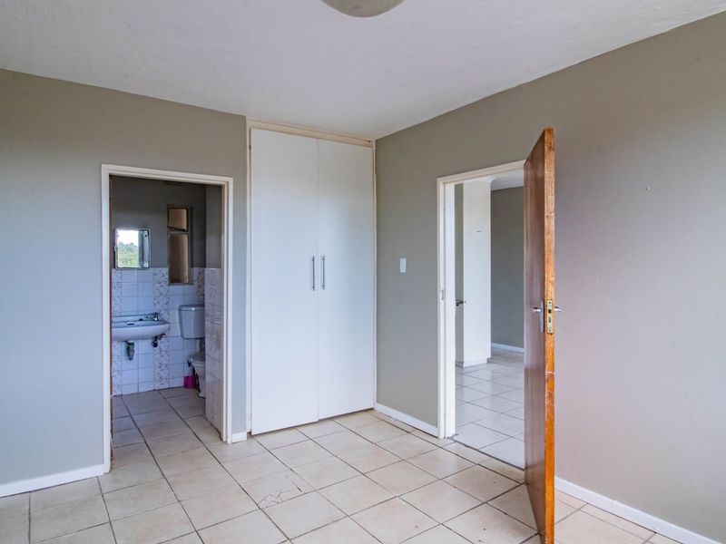 An empty bedroom featuring tiled flooring, a built-in wardrobe, and direct access to an en-suite bathroom.