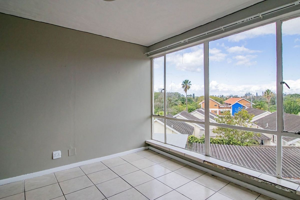 A bright, empty bedroom featuring large windows with neighborhood views and tiled flooring, offering a blank canvas for personalization.