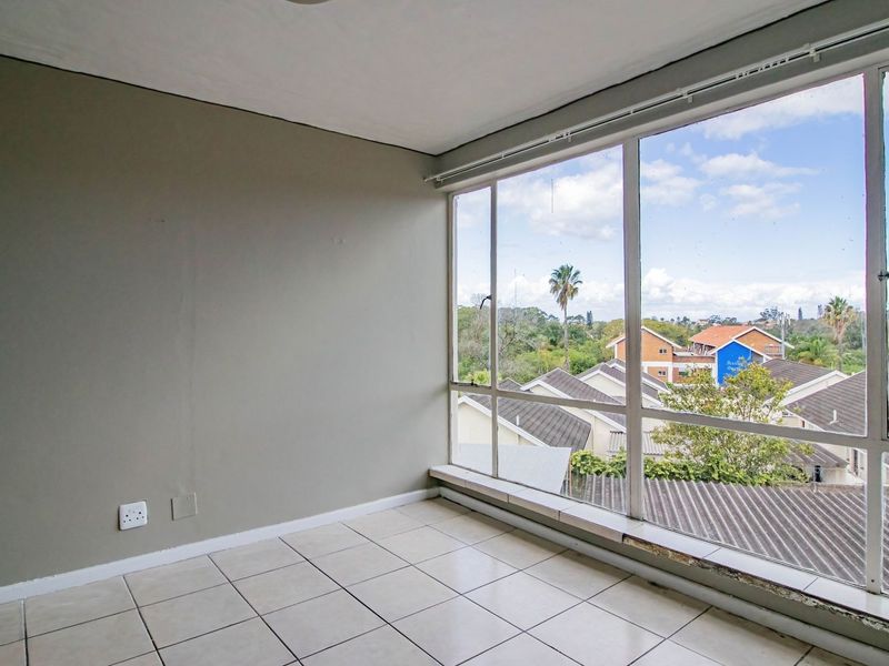 A bright, empty bedroom featuring large windows with neighborhood views and tiled flooring, offering a blank canvas for personalization.