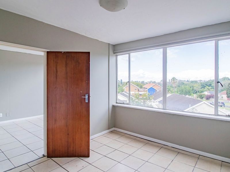 An empty bedroom featuring tiled flooring, a large window with neighborhood views, and a solid wood door leading to an adjacent room.
