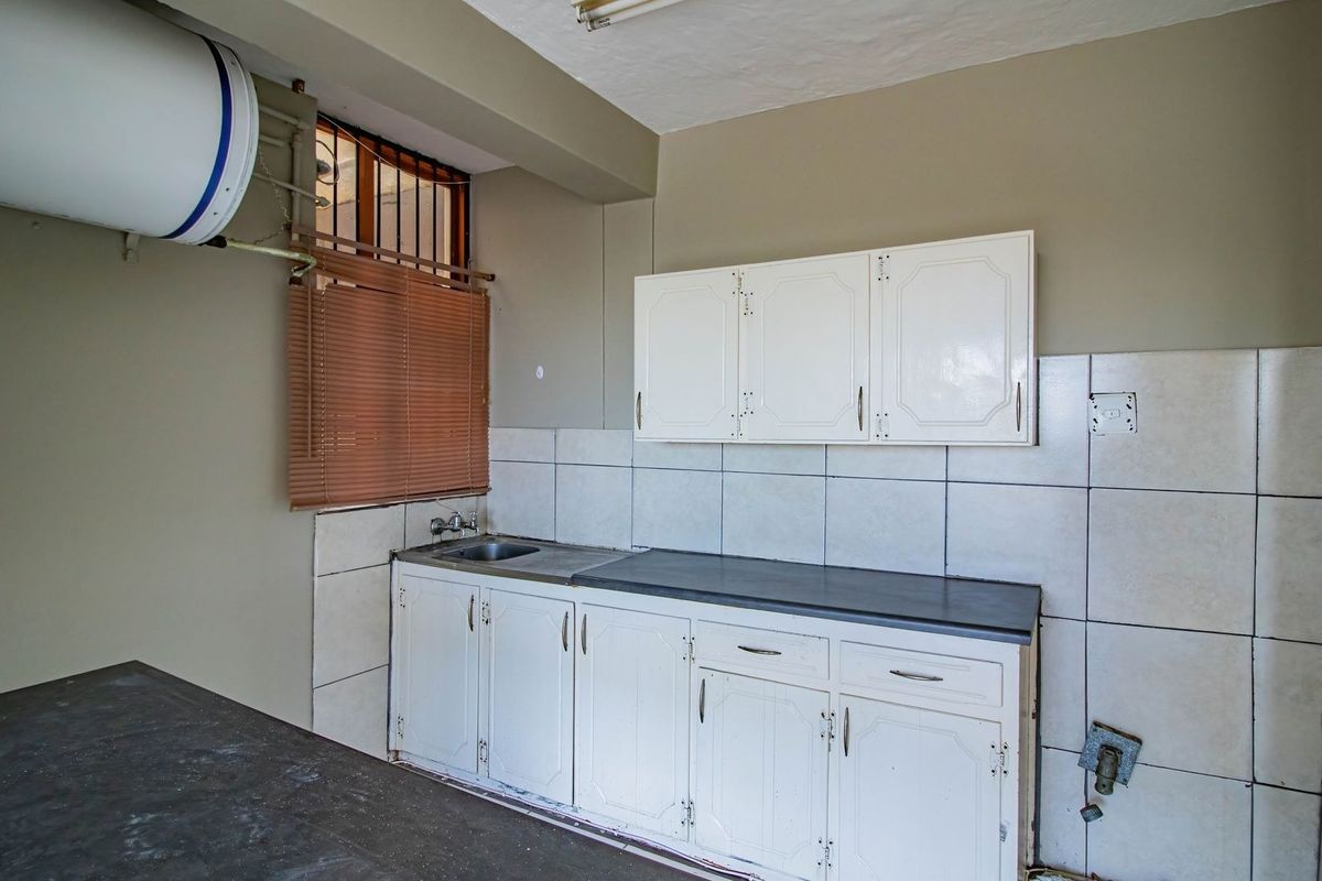 A functional kitchen space featuring built-in white cabinetry, a stainless steel sink, tiled splashbacks, and an electric water heater.