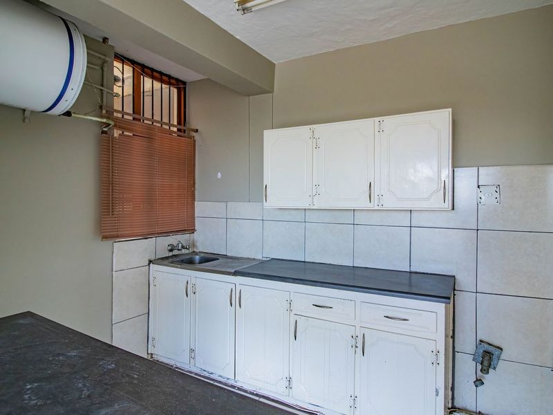 A functional kitchen space featuring built-in white cabinetry, a stainless steel sink, tiled splashbacks, and an electric water heater.