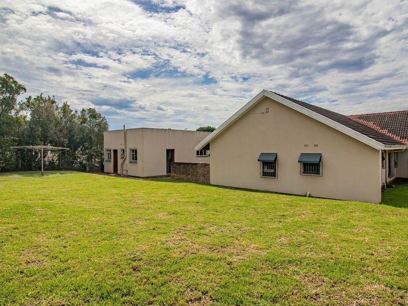 A view of the rear exterior of the house, featuring a large lawn area, tiled roof, and security-fitted windows.