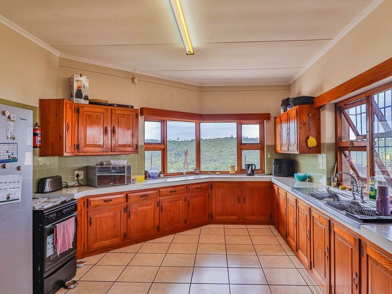 A spacious kitchen featuring traditional wooden cabinetry, tiled flooring, and a large bay window offering scenic views, providing a functional layout with ample storage.