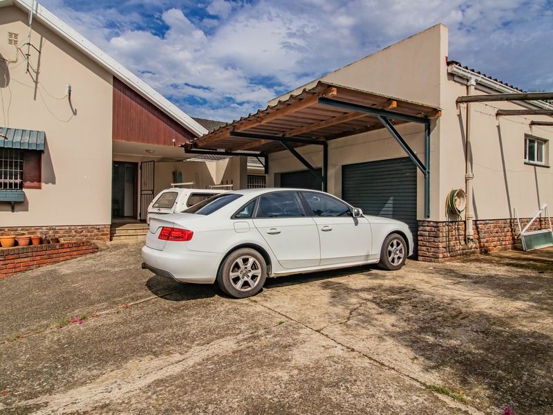 Front exterior view of the house featuring a concrete driveway, a carport, and a garage, showing signs of wear on the driveway and exterior finishes.