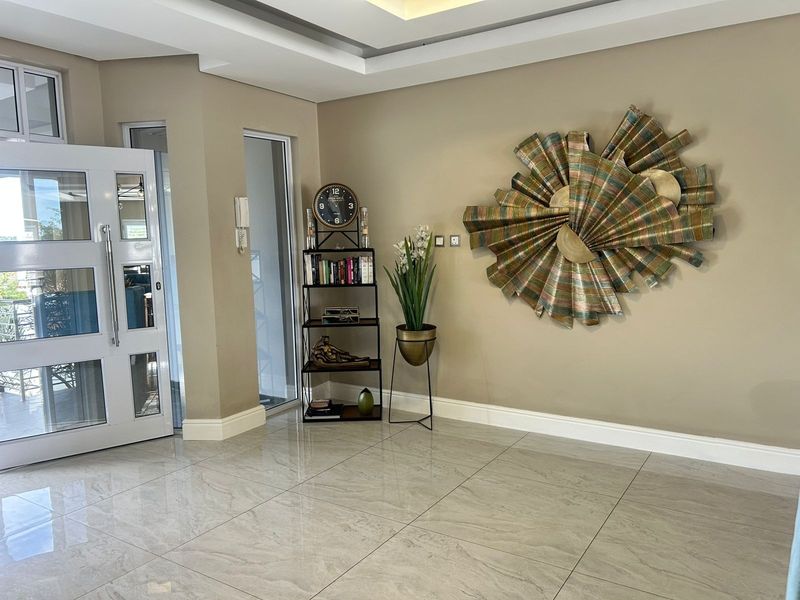 A bright and welcoming entrance hall featuring polished tiled flooring, a modern recessed ceiling design, and a glass-panelled front door.
