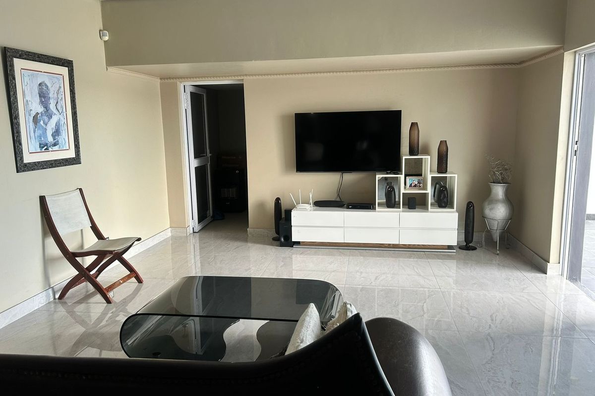 A well-maintained living room featuring polished tile flooring, neutral wall tones, and a sliding glass door providing access to the exterior.
