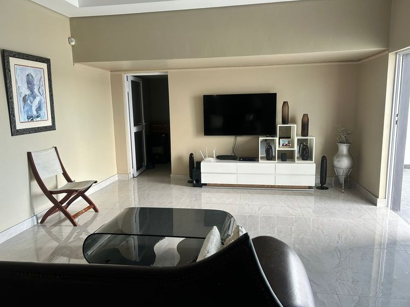 A well-maintained living room featuring polished tile flooring, neutral wall tones, and a sliding glass door providing access to the exterior.