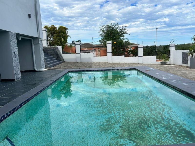 Outdoor pool area featuring a paved deck, perimeter wall with electric fencing, and stone-clad exterior wall details.