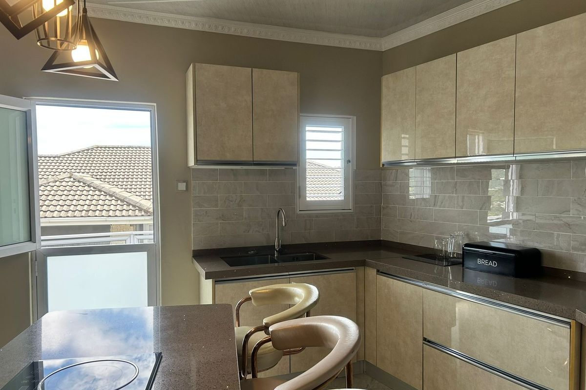 Modern kitchen featuring high-gloss cabinetry, stone countertops, integrated induction hob, tiled backsplash, and stylish pendant lighting with access to an outdoor balcony.