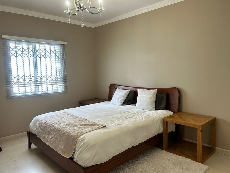 A well-maintained bedroom featuring laminate flooring, crown molding, a decorative chandelier, and a window fitted with a security gate and venetian blinds.