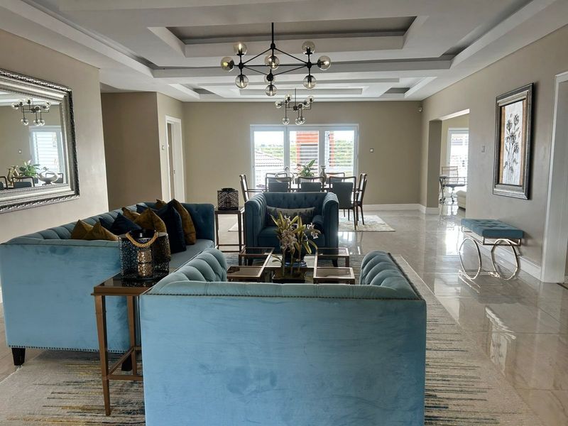 Spacious open-plan living and dining area featuring a sophisticated tray ceiling, modern lighting fixtures, and high-gloss polished floor tiles.