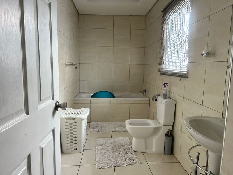 A functional bathroom featuring neutral ceramic wall and floor tiles, a built-in bathtub, a pedestal washbasin, and a toilet.
