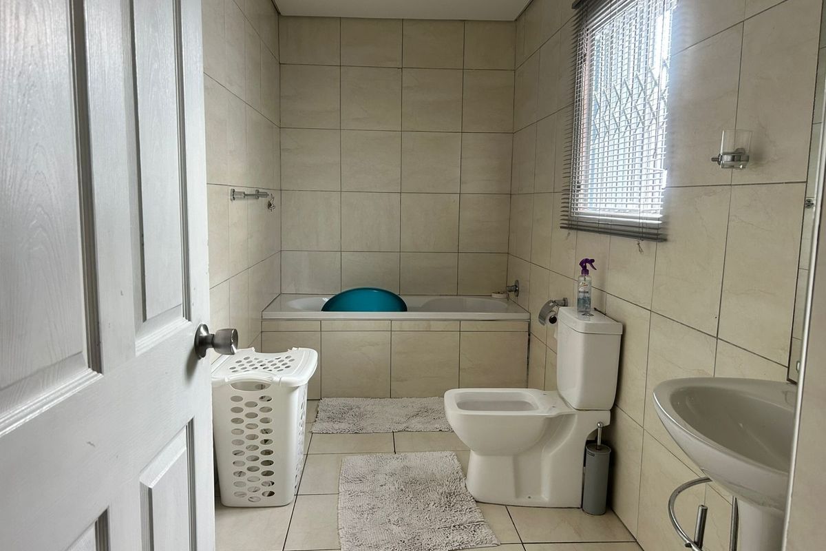 A functional bathroom featuring neutral ceramic wall and floor tiles, a built-in bathtub, a pedestal washbasin, and a toilet.