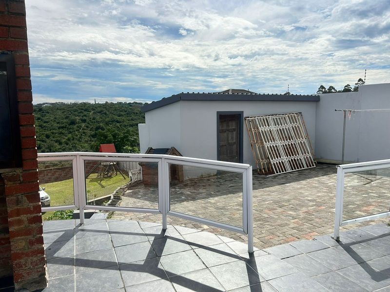 An elevated outdoor patio area featuring tiled flooring, a glass balustrade, and views over the rear garden and surrounding landscape.