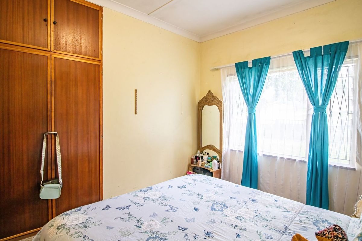 A bedroom featuring a built-in wooden wardrobe and a window fitted with security bars, offering a functional space with potential for cosmetic updates.