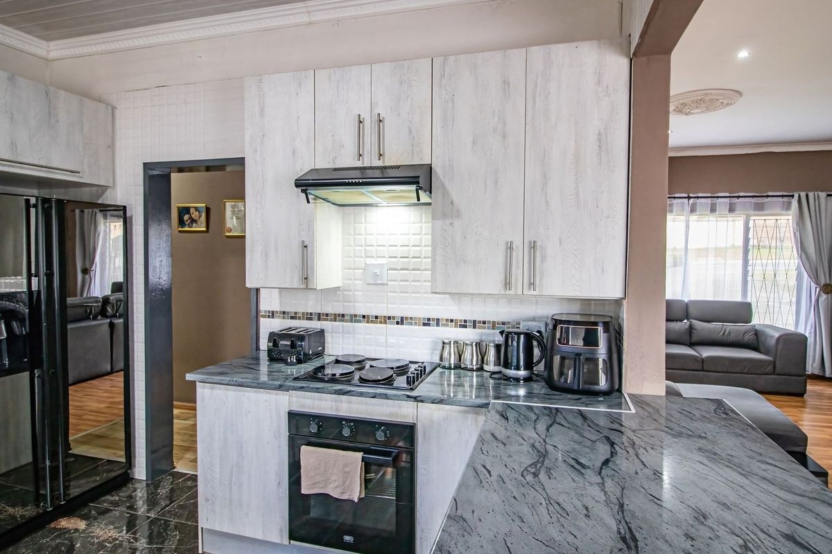 Modern kitchen featuring light wood-grain cabinetry, dark stone countertops, built-in oven, electric hob, and a tiled backsplash, seamlessly connected to the living area.