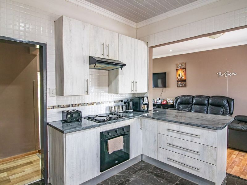 Open-plan kitchen featuring light wood-grain cabinetry, dark stone-look countertops, and integrated appliances, flowing into an adjacent living area.