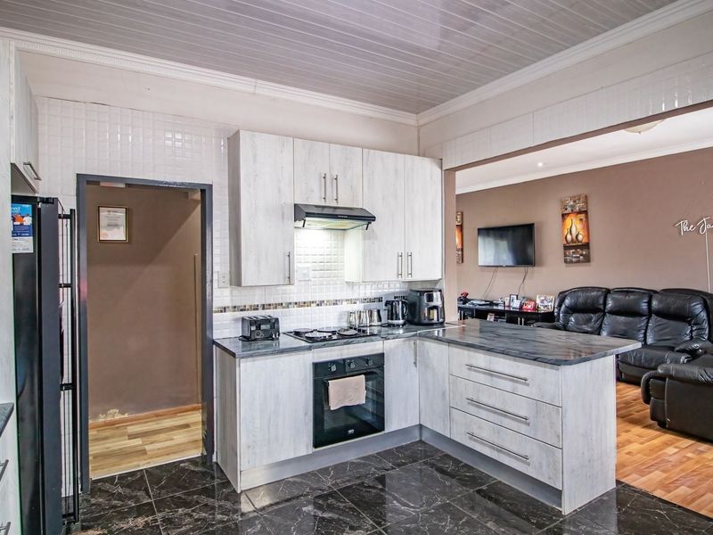 Open-plan kitchen featuring modern light-wood cabinetry, dark stone-look countertops, and integrated appliances, flowing seamlessly into the adjacent living area.