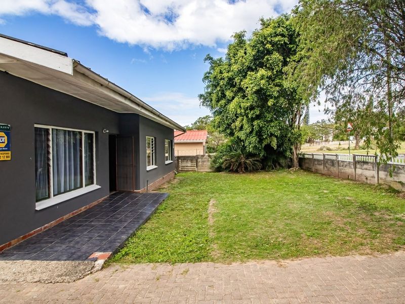Rear exterior view of the property featuring a tiled patio area, paved driveway, and a private garden enclosed by a perimeter wall.