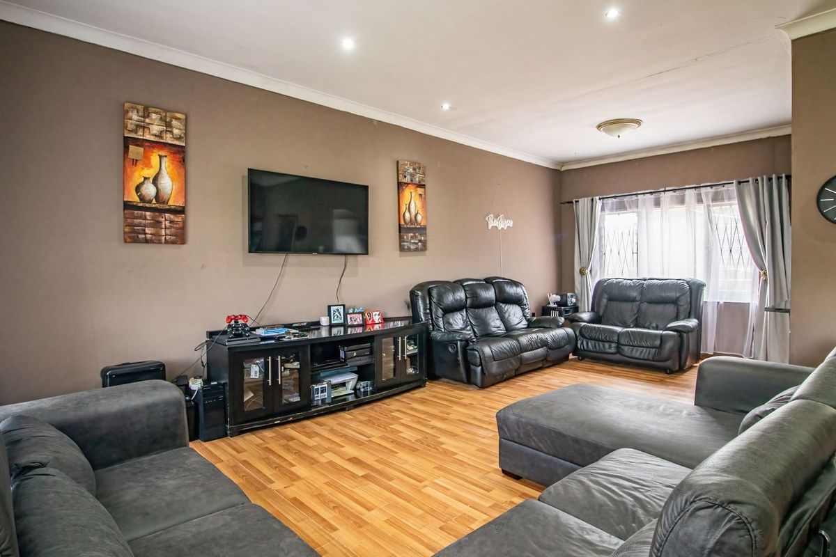 A spacious living room featuring laminate flooring, recessed downlighting, and coved cornicing, providing a comfortable and functional family area.