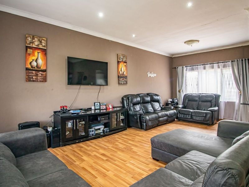 A spacious living room featuring laminate flooring, recessed downlighting, and coved cornicing, providing a comfortable and functional family area.