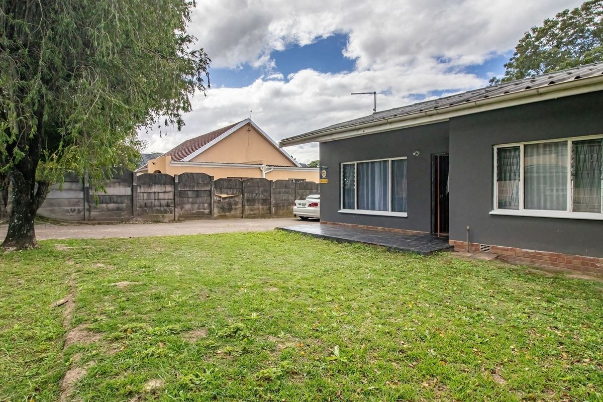 Rear view of the property featuring a dark grey exterior finish, a small tiled patio area, and a spacious lawn enclosed by a boundary wall.