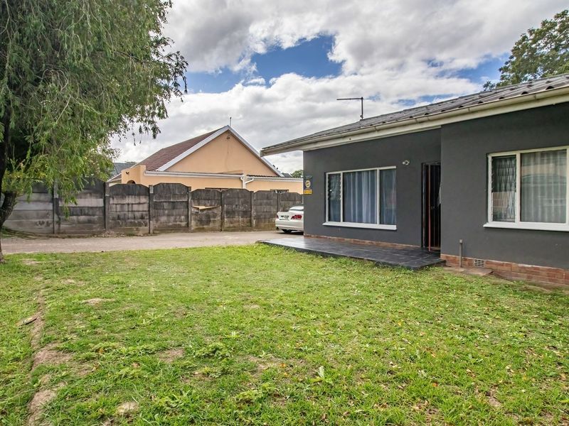 Rear view of the property featuring a dark grey exterior finish, a small tiled patio area, and a spacious lawn enclosed by a boundary wall.