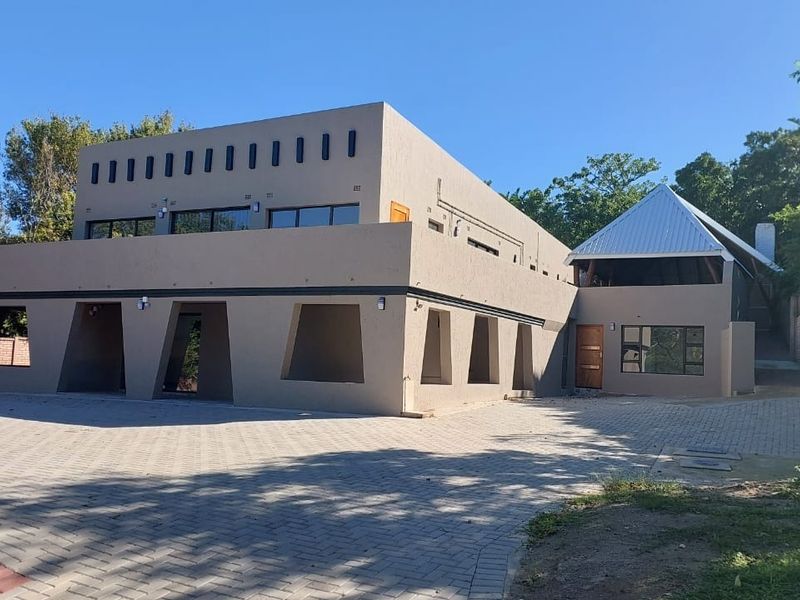 Front view of a modern multi-level house featuring a paved driveway, stucco exterior, and a distinctive metal roof structure.