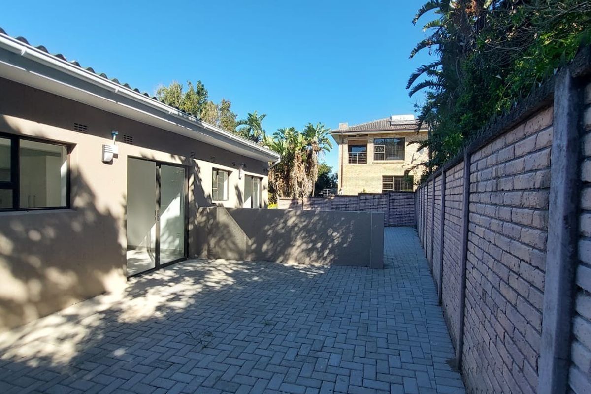 A well-maintained rear exterior area featuring a paved patio, sliding door access to the home, and a secure brick boundary wall.