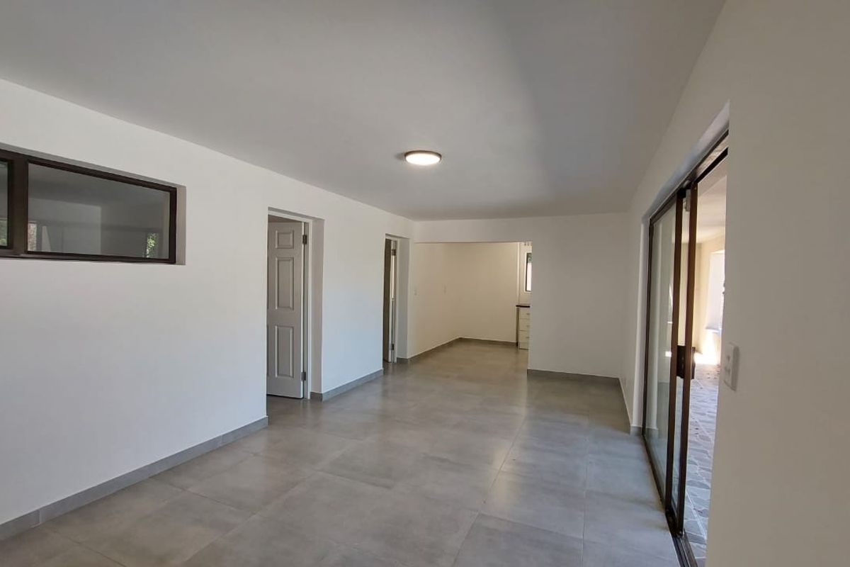 A bright, open-plan living area featuring neutral tiled flooring, clean white walls, and large sliding glass doors providing natural light and outdoor access.
