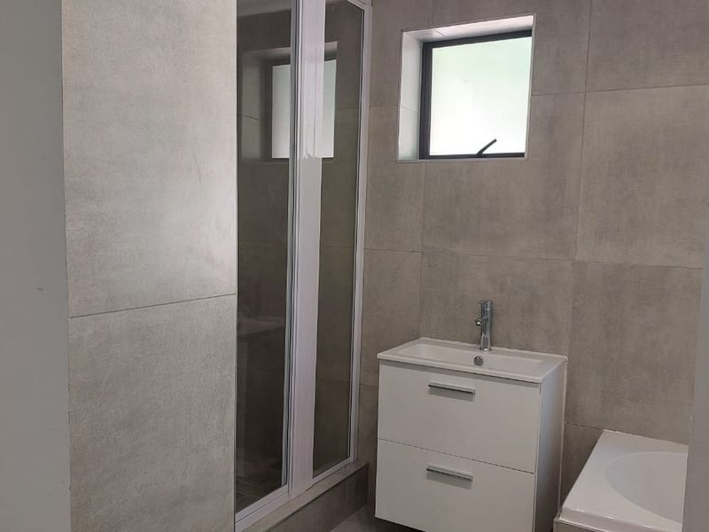 Modern bathroom featuring grey wall tiles, a white vanity cabinet with basin, and a glass-enclosed shower.