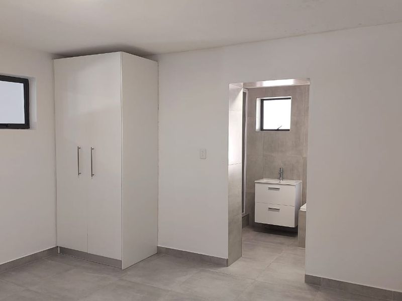 A clean, modern bedroom featuring neutral tiled flooring, a built-in wardrobe, and direct access to an en-suite bathroom with a contemporary vanity.