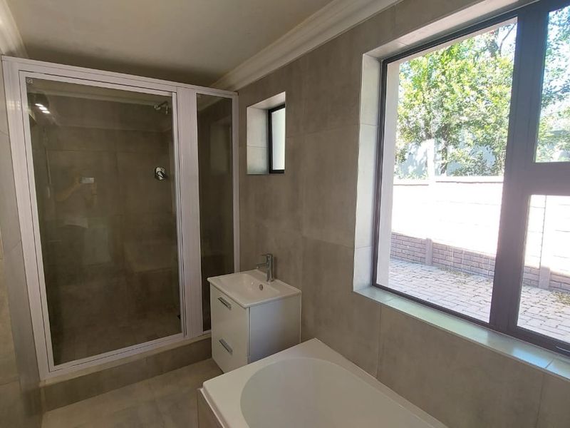 Modern bathroom featuring a glass shower enclosure, vanity basin, and bathtub with large windows providing natural light and garden views.