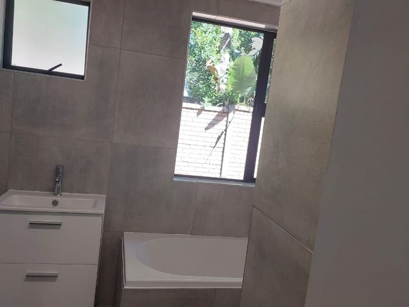 Modern bathroom featuring large format grey wall tiles, a white built-in vanity with basin, and a built-in bathtub.