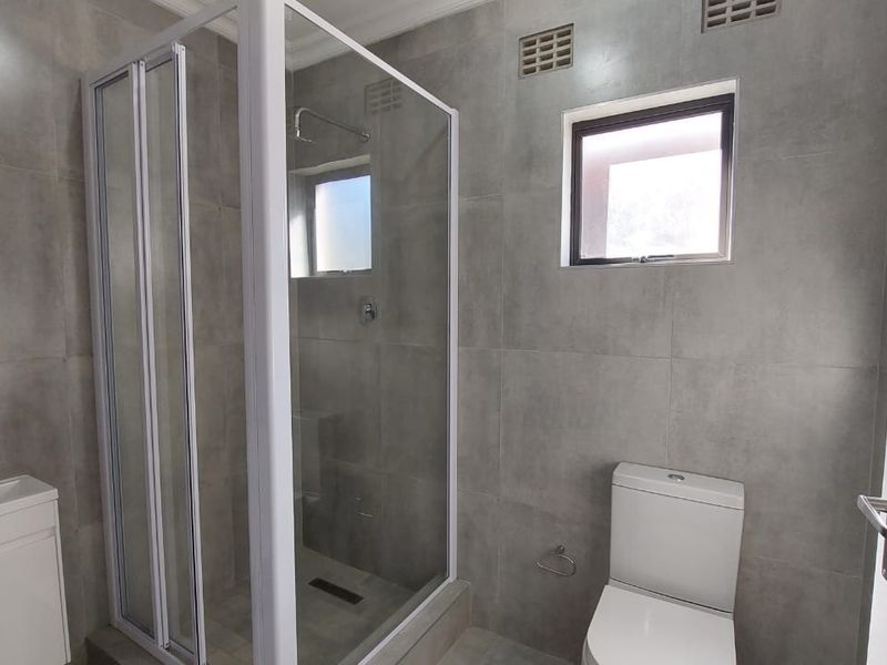 Modern bathroom featuring grey floor-to-ceiling tiles, a glass shower enclosure, a white vanity basin, and a standard toilet.
