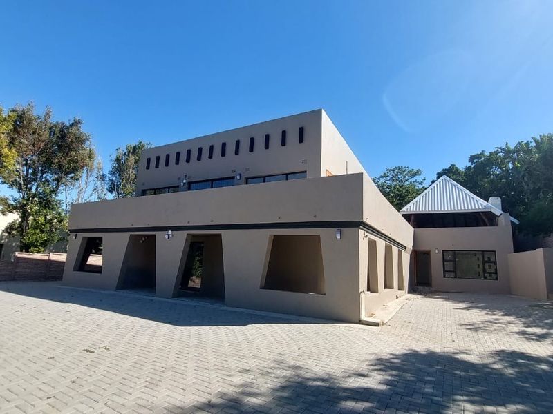 A modern, multi-level residential property featuring a large paved driveway, contemporary architectural facade, and secure boundary walling.