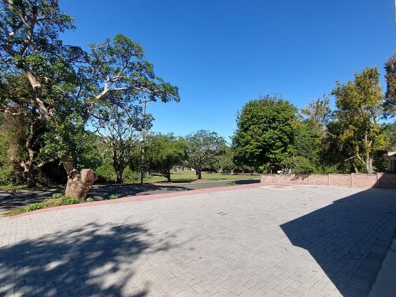 A spacious paved driveway area leading to the property, featuring a brick boundary wall and mature surrounding trees.