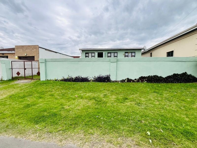 Front view of the property featuring a green perimeter wall, metal gate, and a well-maintained lawn area.