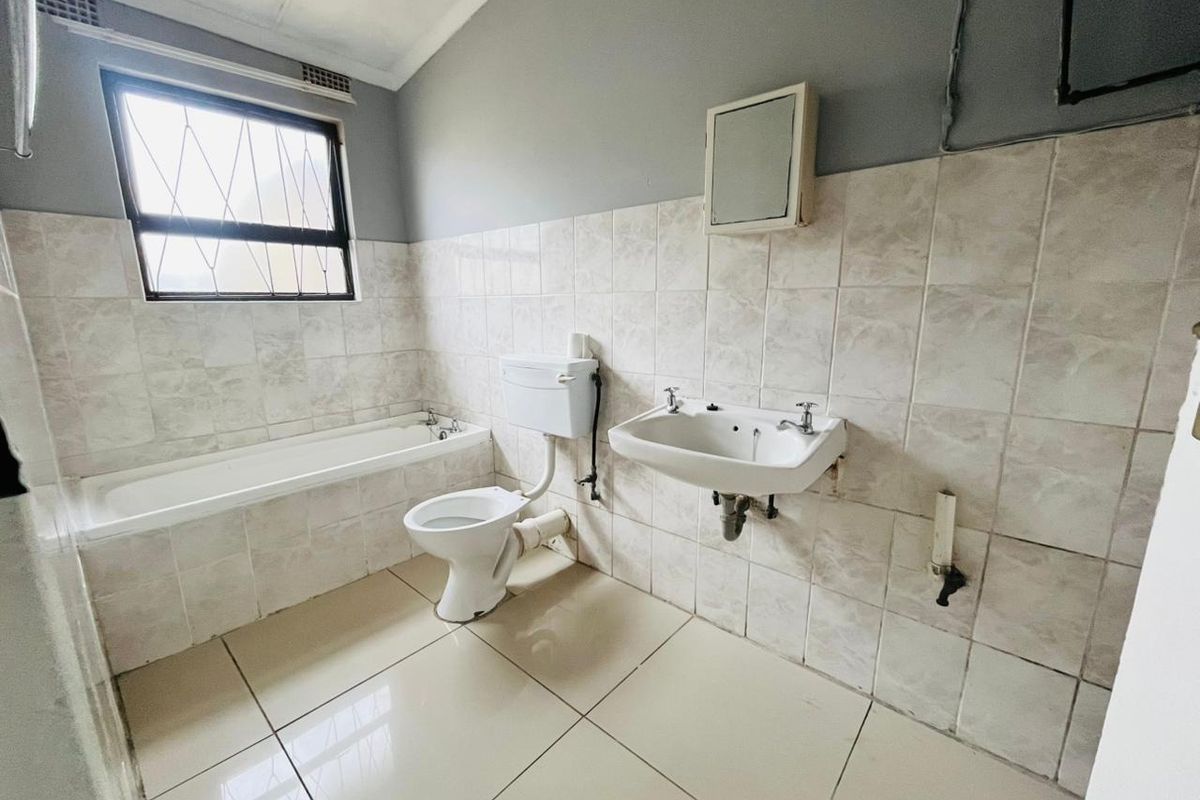 A functional bathroom featuring a bathtub, wall-mounted basin, and toilet, finished with neutral wall and floor tiles. The space is ready for modernization.
