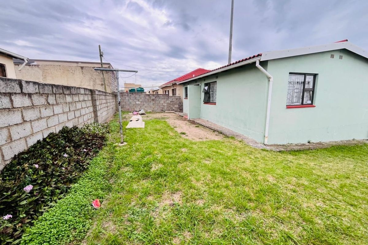 Rear view of the property featuring a grassed garden area, concrete block boundary walls, and exterior building facade with metal window frames.